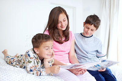 Buy stock photo Three siblings reading a magazine together happily in bed