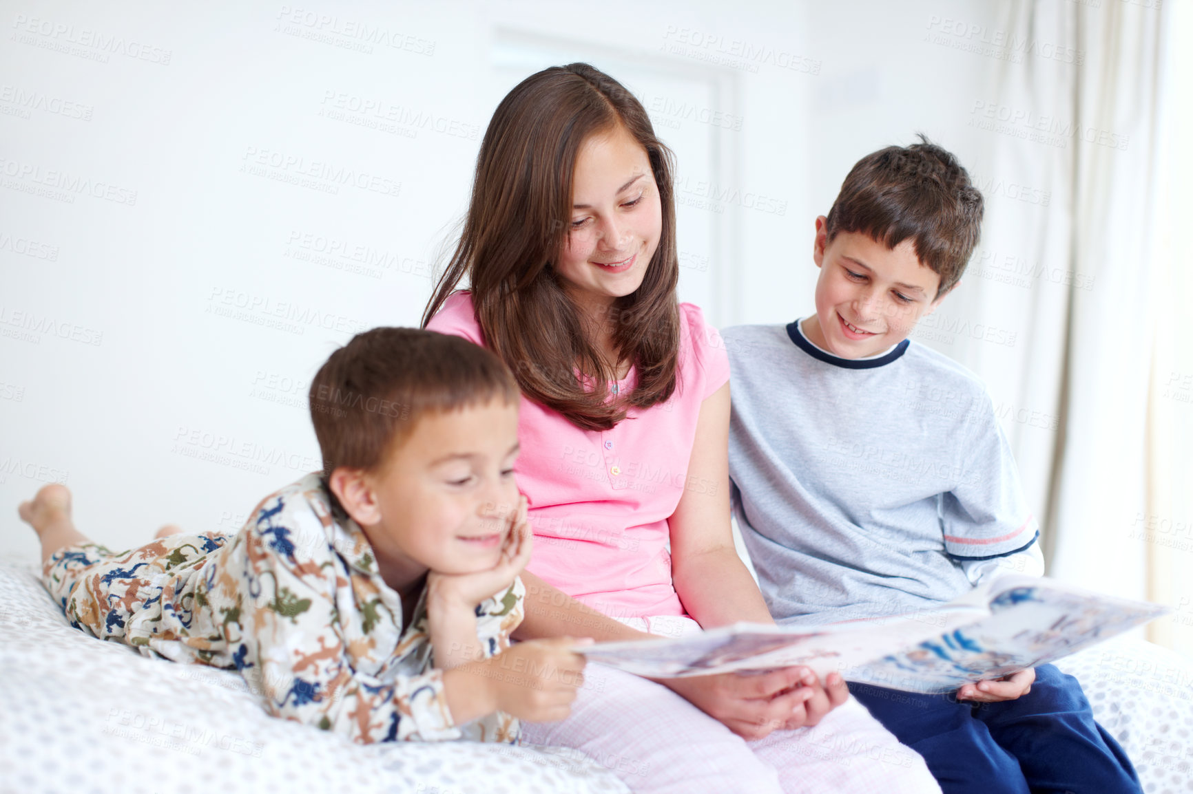 Buy stock photo Three siblings reading a magazine together happily in bed