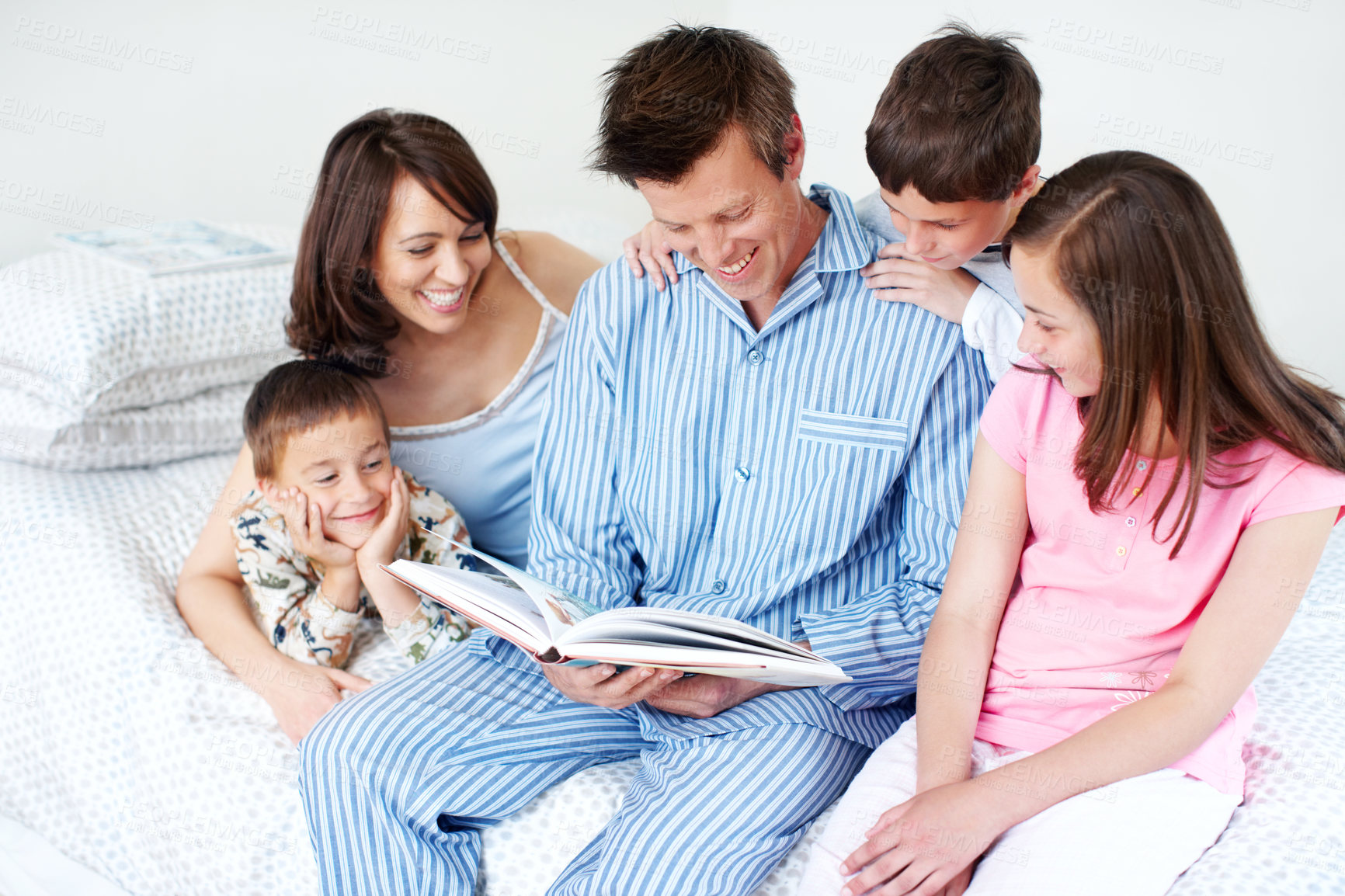 Buy stock photo A loving family of five reading on a bed together