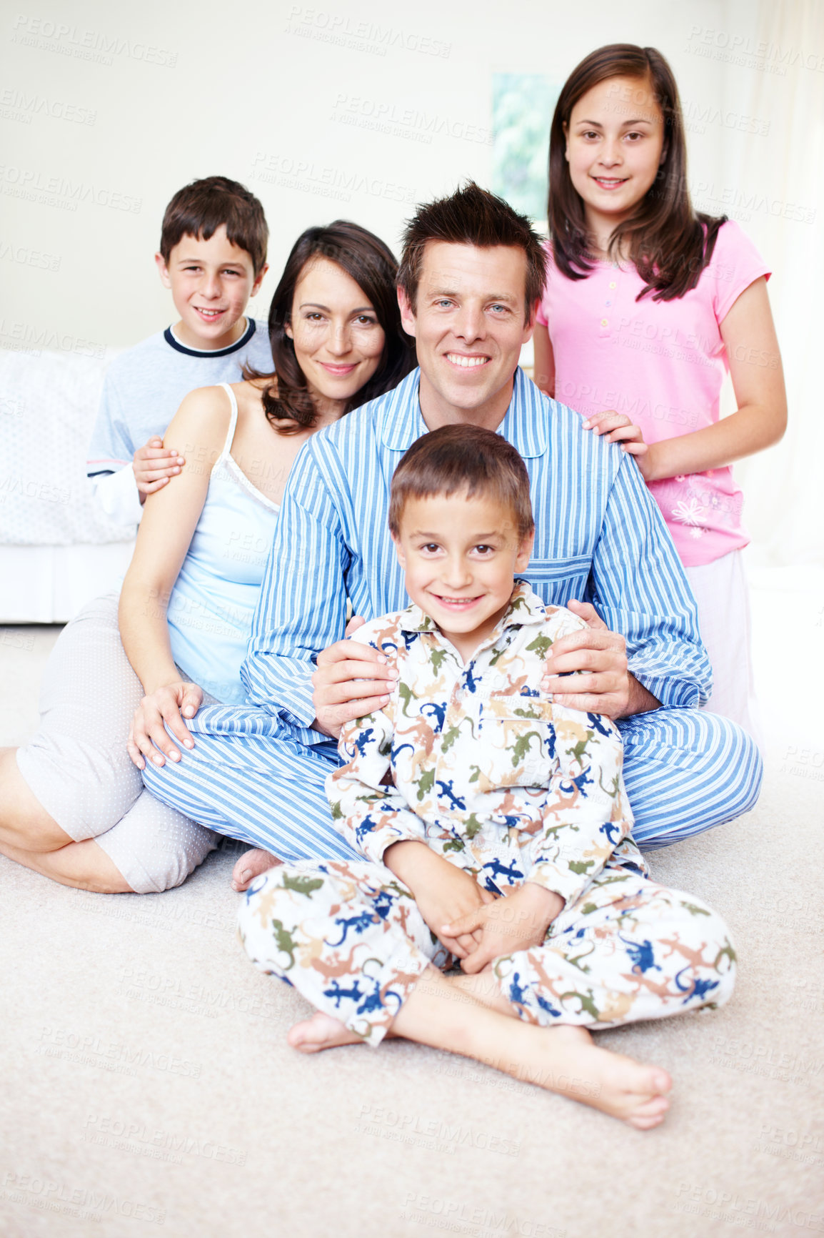 Buy stock photo Portrait of a cute little boy with his family sitting behind him happily on a bed