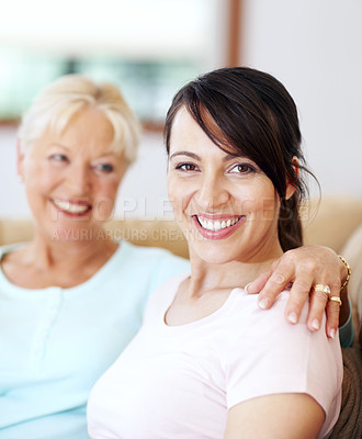 Buy stock photo Portrait of beautiful smiling woman sitting with her mother. Attractive brunette feeling happy on couch with her senior parent. Aged mother with her arm around her adult child spending time together 