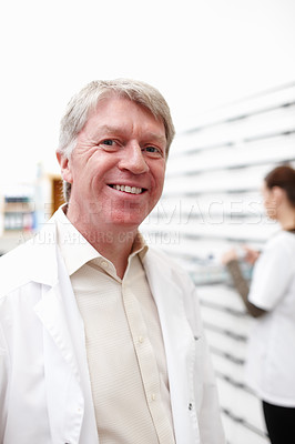 Buy stock photo Portrait of handsome mature pharmacist smiling with colleague working in background