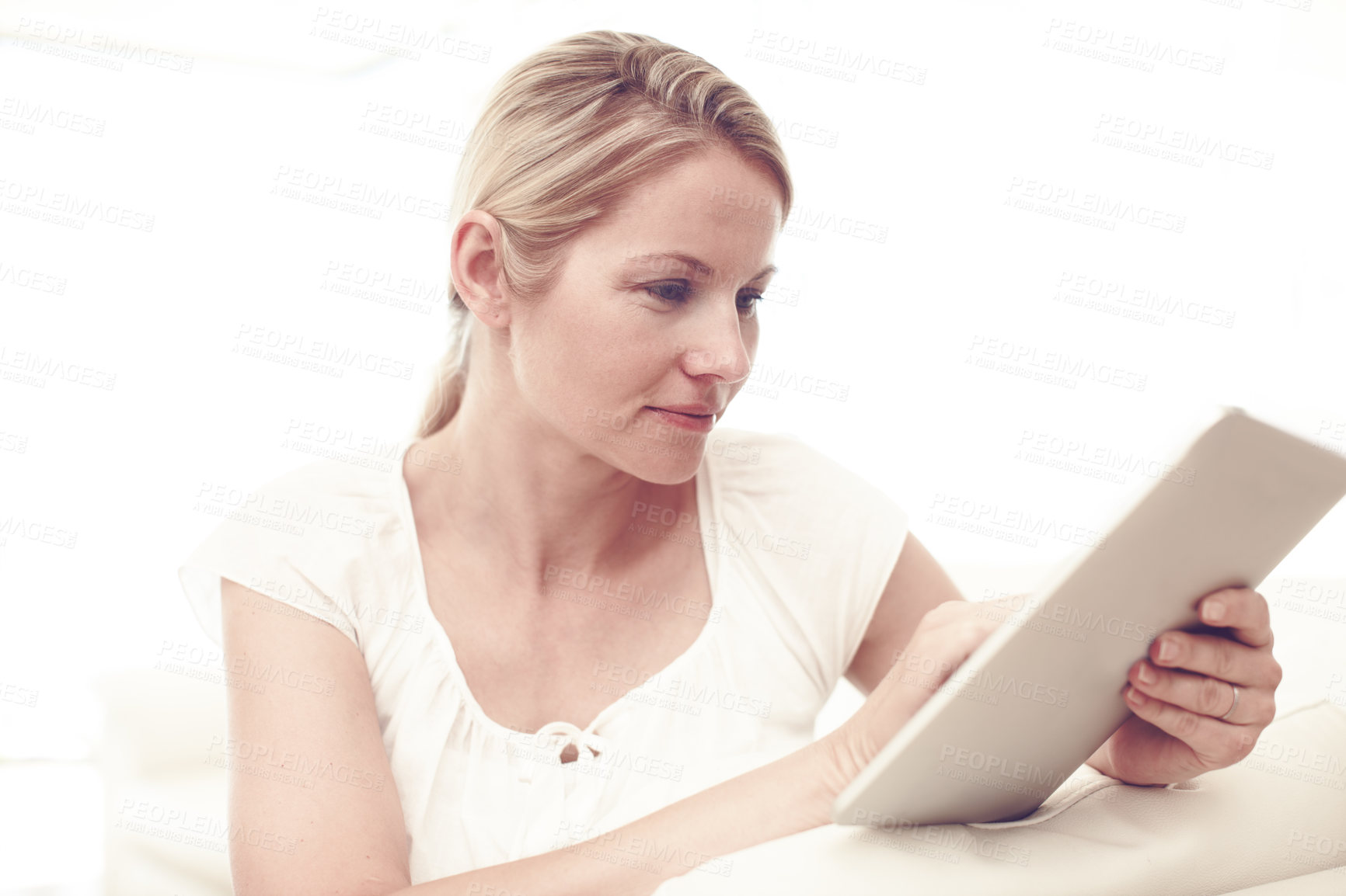 Buy stock photo An attractive blonde woman using a tablet while sitting at home
