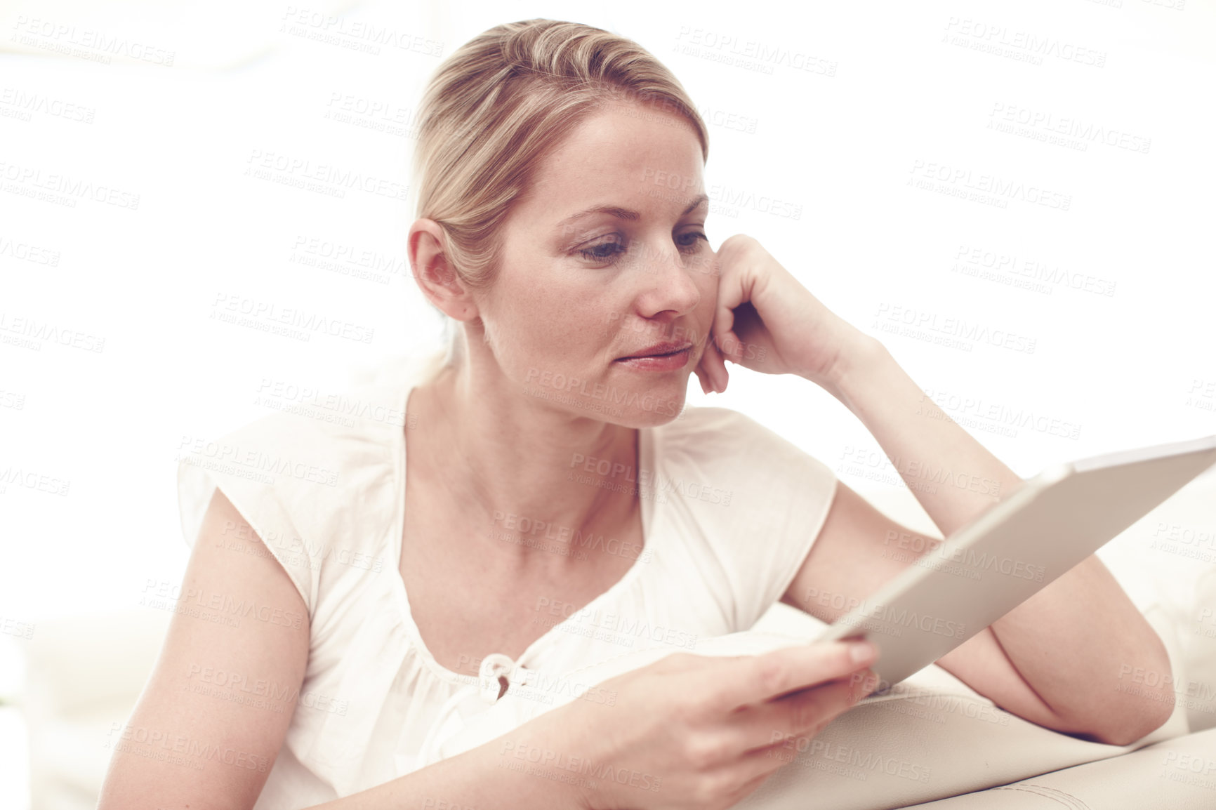 Buy stock photo An attractive blonde woman using a tablet while sitting at home