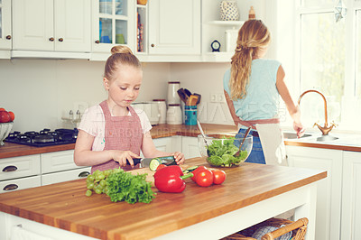 Buy stock photo A little girl making a salad in the kitchen with her mother standing nearby