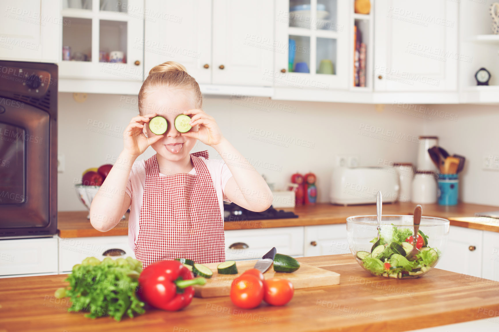 Buy stock photo Vegetables, cucumber on eyes and silly kid in kitchen for healthy eating, wellness and vegetarian diet. Food, home and goofy and young girl with organic ingredients for lunch, dinner and meal prep