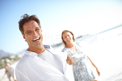 Buy stock photo Portrait of a happy mature woman leading her husband by the hand while walking on the beach together