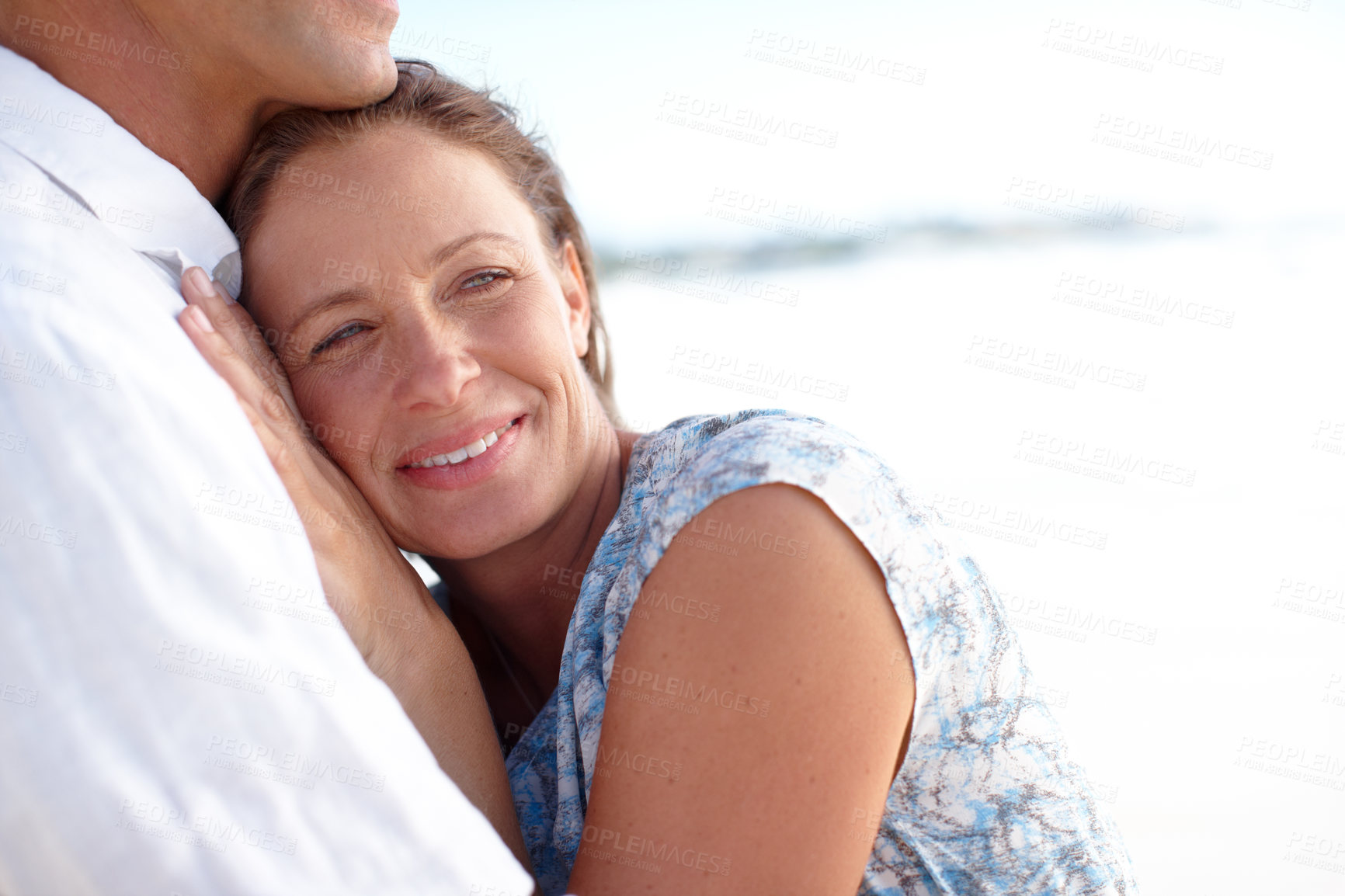Buy stock photo A mature man embracing his happy wife from behind as they stand on the beach