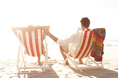 Buy stock photo Rear view of a couple sitting in deck chairs on the beach together