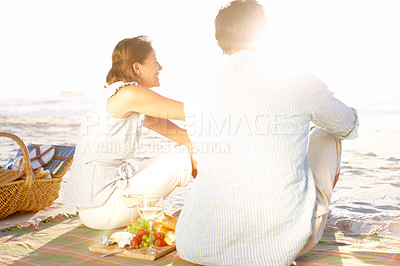 Buy stock photo A loving couple watching the sunset while enjoying a picnic together on the beach