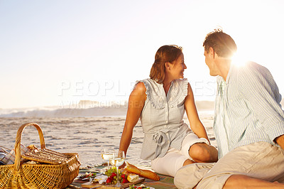 Buy stock photo A loving couple watching a sunset on the beach while enjoying a picnic