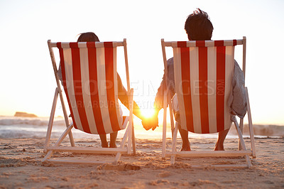 Buy stock photo Couple, back and holding hands on beach for sunset, bonding and holiday on anniversary date with sunshine. Man, woman and travel by ocean for trip, love and tropical vacation with chair in Maldives