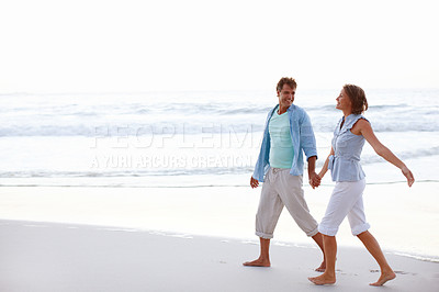 Buy stock photo A happy couple walking hand in hand on the beach together