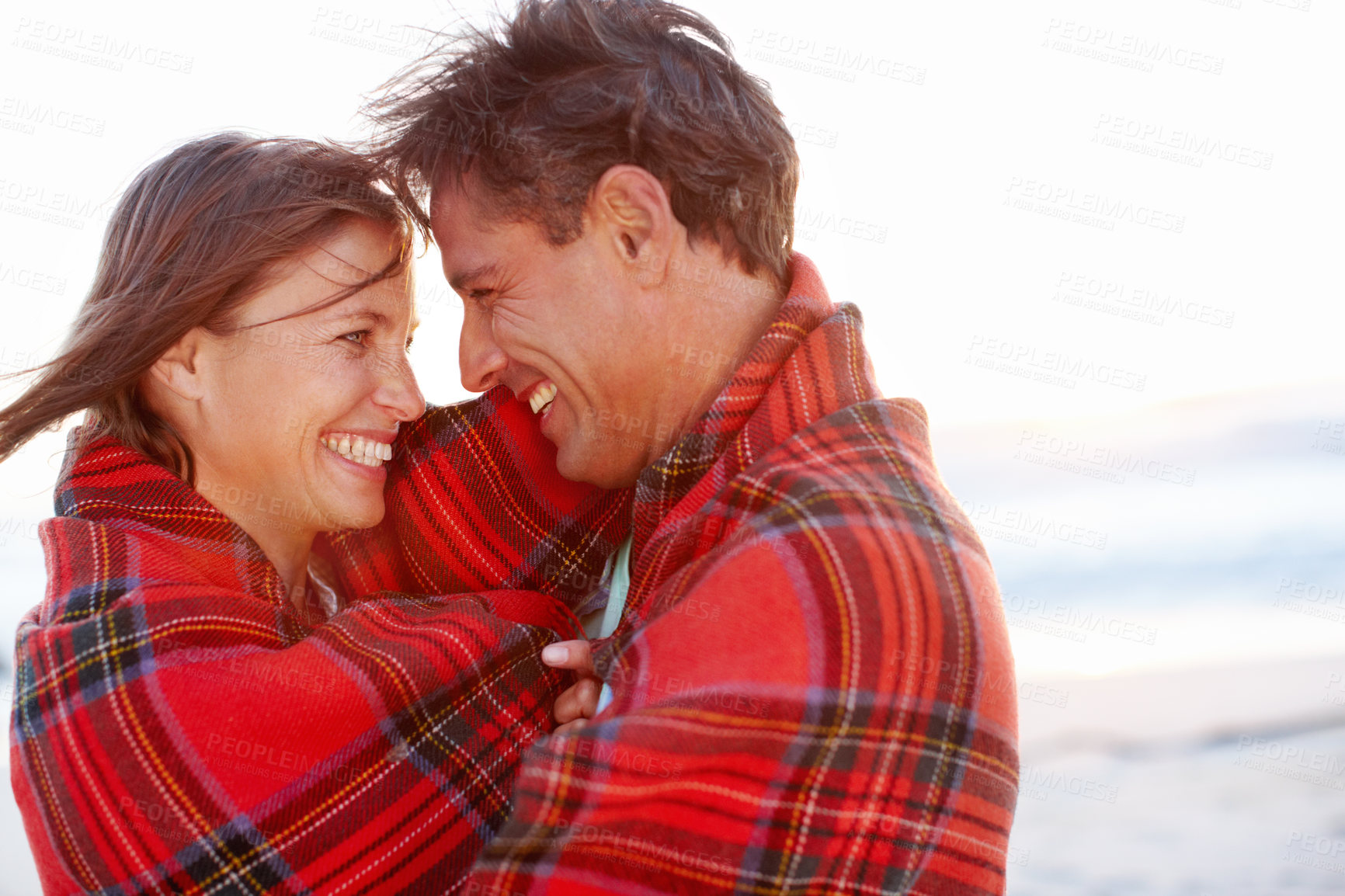 Buy stock photo Laughing, blanket or happy couple hug at sea for love on vacation, anniversary or honeymoon holiday. Funny joke, cold or people with smile, care or romance at ocean together for beach and bonding