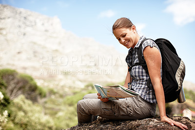 Buy stock photo One happy young woman reading a map while taking a break from exploring and hiking along a mountain trail outdoors. Adventurous female hiker navigating directions for route along trek expedition 