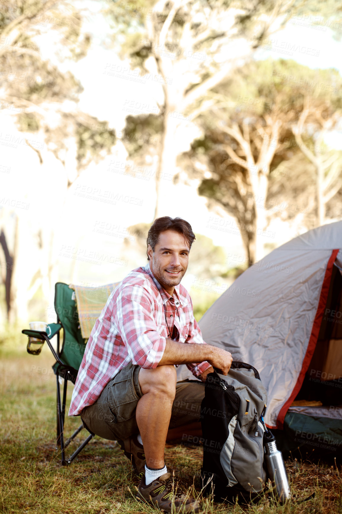 Buy stock photo Man, smile and portrait on camping chair by tent, outdoor and bag on adventure, journey or holiday in summer. Person, relax and backpack on grass field for vacation, sunshine and happy in Argentina