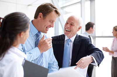 Buy stock photo Laughing businesspeople going through documents together in an informal meeting 