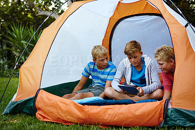 Buy stock photo Shot of three young boys using a digital tablet while in their tent