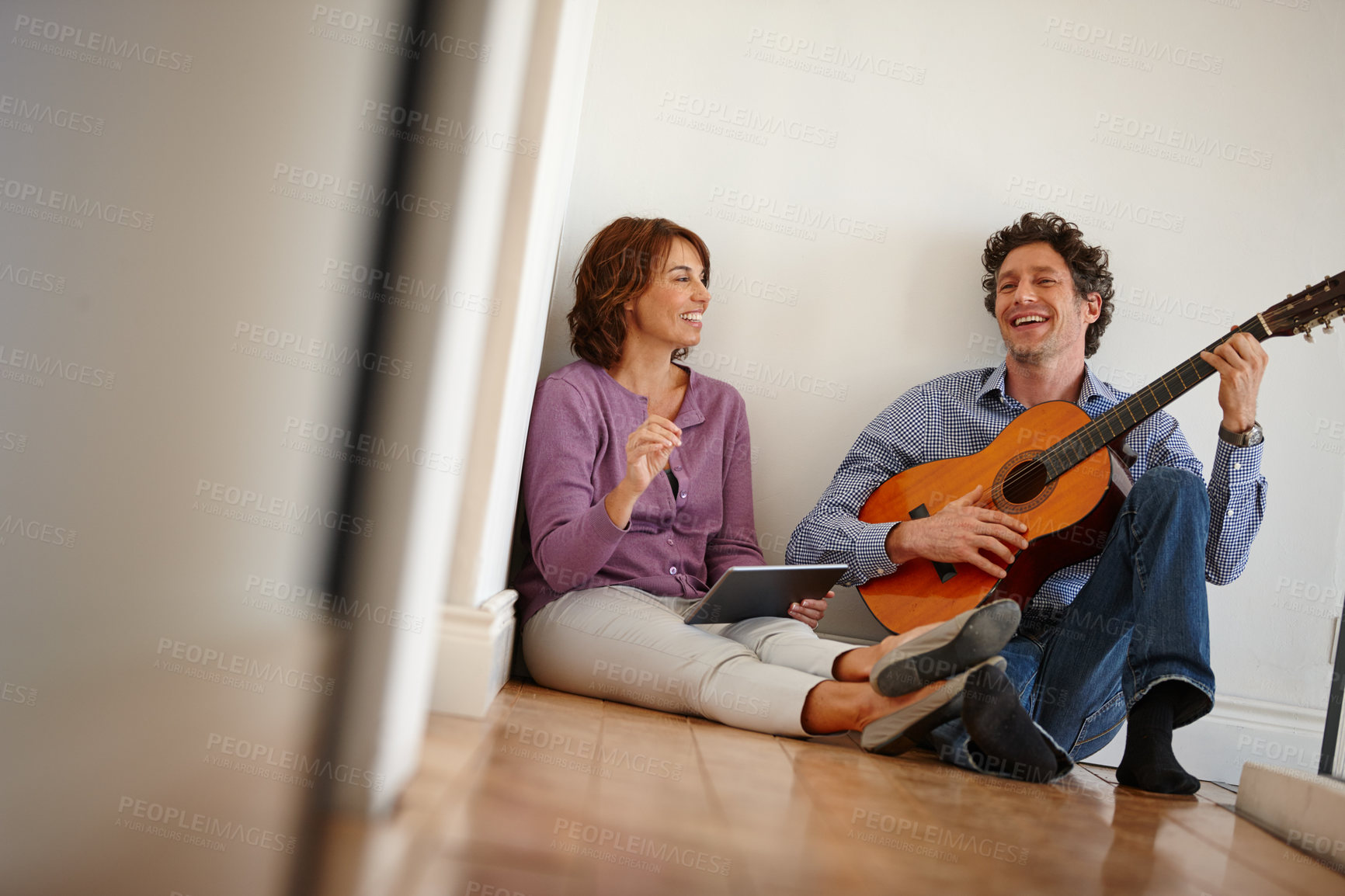 Buy stock photo Shot of a woman using her digital tablet while her husband plays the guitar