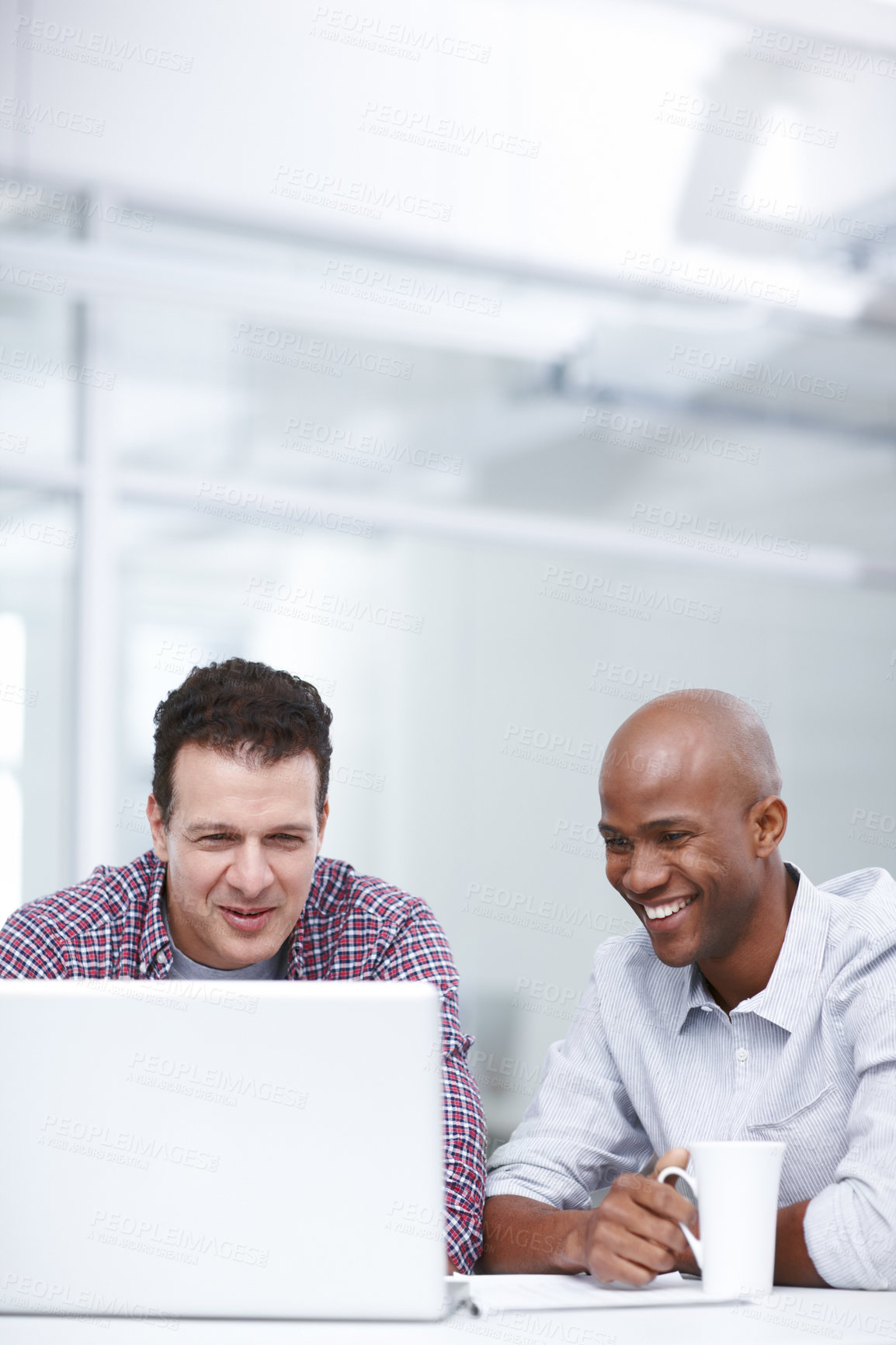 Buy stock photo Two businessmen looking at something on their laptop screen while they're seated at a table