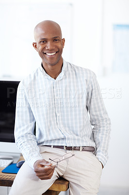 Buy stock photo Portrait of a smiling african american businessman sitting on a computer desk and smiling at the camera