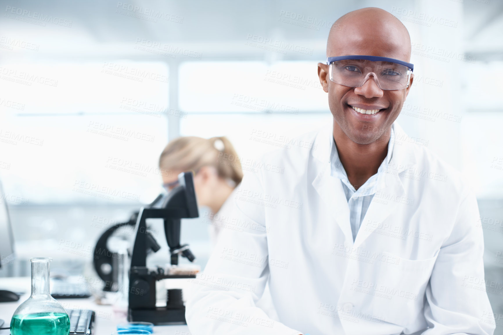 Buy stock photo Portrait of a smiling young chemist in the lab with a female coworker in the background