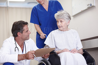Buy stock photo A female nurse pushing a senior patient in a wheelchair down the hallway while talking with her doctor
