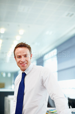 Buy stock photo Portrait of a happy young male executive in his workplace. A young talented caucasian business person with a blue tie and white shirt standing in corporate office looking around and confident