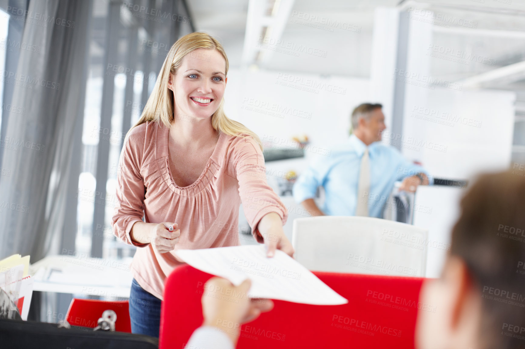 Buy stock photo A young female office worker handing a colleague a document with her boss standing in the background