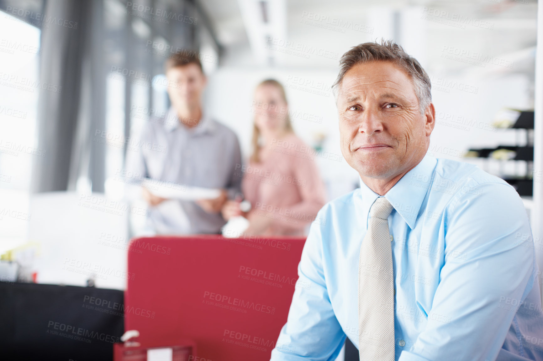 Buy stock photo Portrait of a senior business manager smiling while his colleagues work in the background