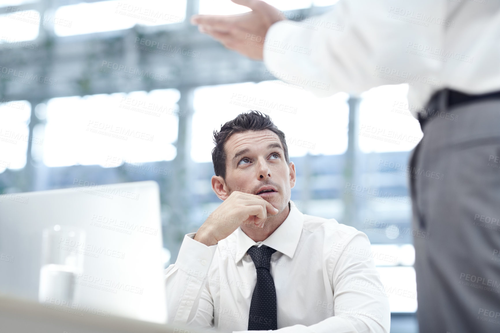 Buy stock photo A businessman sitting down at a laptop and looking up to a colleague as they discuss business