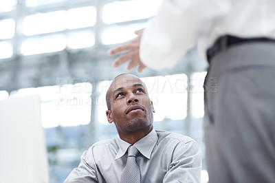 Buy stock photo A businessman sitting down in front of his notebook and looking up to a colleague as they discuss business