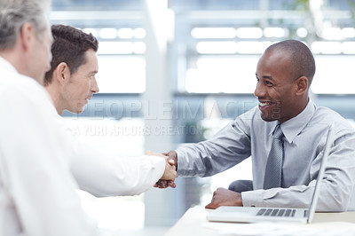 Buy stock photo Three businessmen sitting down as two of them shake hands in agreement
