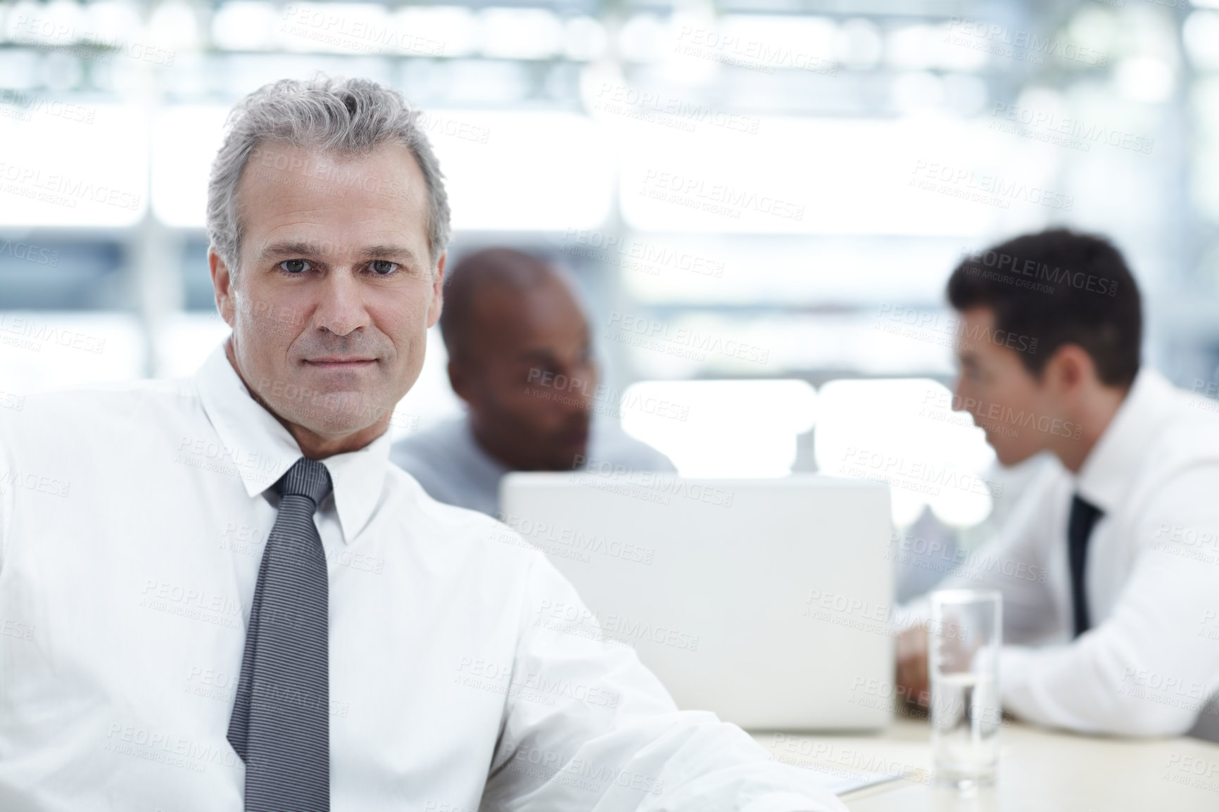 Buy stock photo Portrait of a mature businessman sitting in front of two younger colleagues