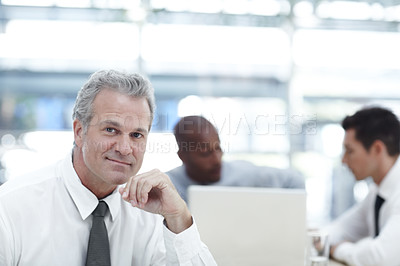 Buy stock photo Portrait of a mature businessman sitting in front of two younger coworkers