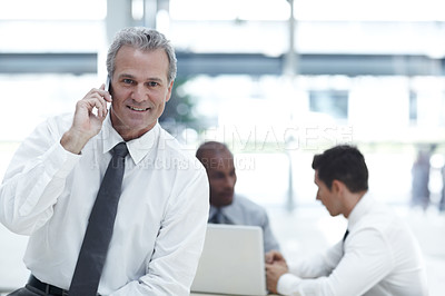 Buy stock photo Portrait of a mature businessman talking on his cellphone in front of two younger colleagues