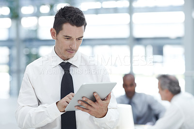 Buy stock photo A young businessman using his digital tablet in front of two  colleagues