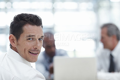 Buy stock photo Handsome businessman looking over his shoulder at the camera and smiling with colleagues working in the background