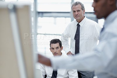 Buy stock photo Businessmen watch as a colleague delivers at presentation on a flipchart