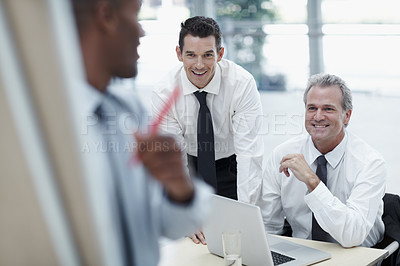 Buy stock photo Businessmen smile and watch as a colleague writes on a flipchart