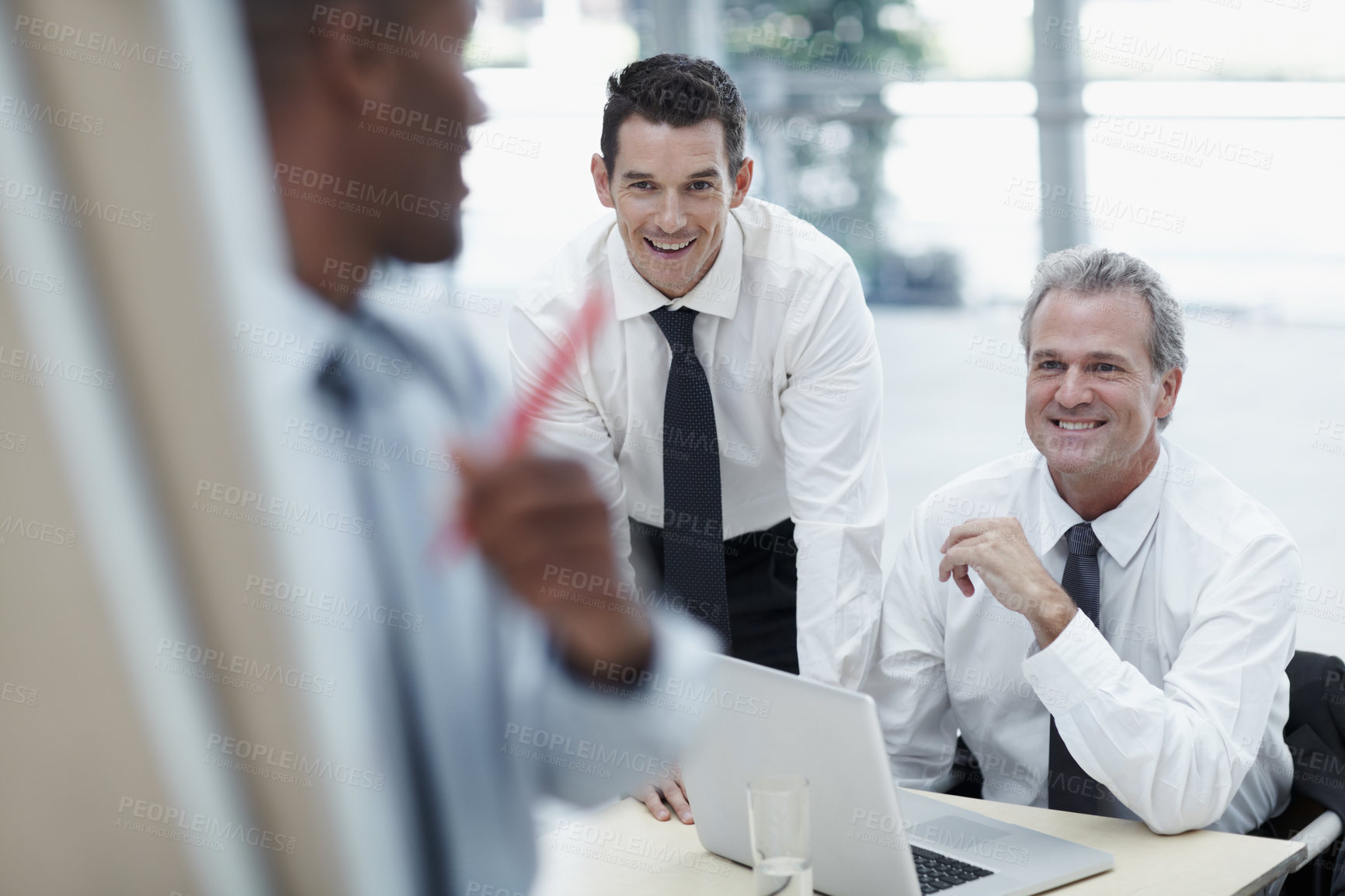 Buy stock photo Businessmen smile and watch as a colleague writes on a flipchart