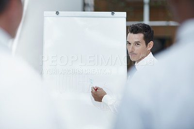 Buy stock photo A businessman writing on flipchart with colleagues watching in the foreground