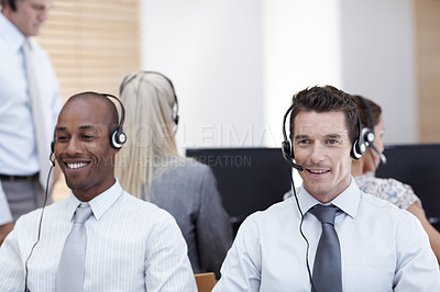 Buy stock photo Two handsome customer service representatives sit and work with colleagues in the background