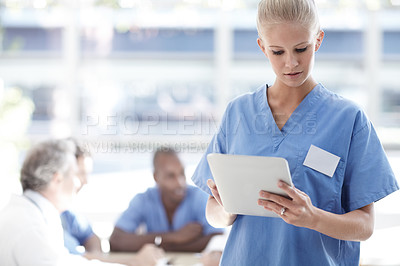 Buy stock photo Medical professional standing and using a touchpad with colleagues sitting in the background