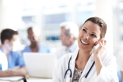 Buy stock photo A beautiful medical professional talking on her cellphone with colleagues working in the background