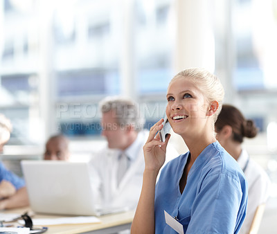 Buy stock photo A beautiful medical professional talking on her cellphone with colleagues working in the background