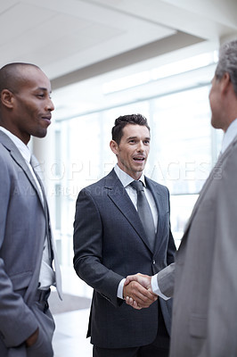 Buy stock photo A mature businessman shaking hands with a younger businessman while another looks on