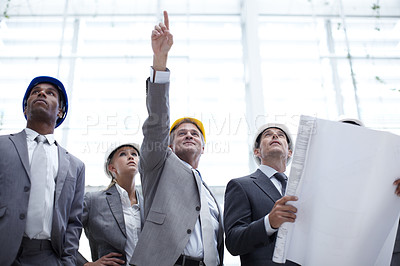 Buy stock photo A shot of a diverse group of engineering professionals pointing up at a building while holding blueprints