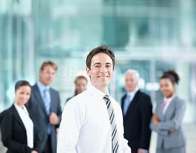 Buy stock photo Handsome young business associate smiling with his colleagues in the background - portrait 