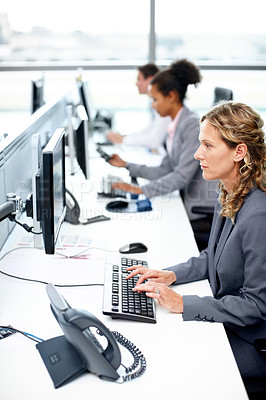 Buy stock photo Profile view of a serious businesswoman working on her computer with her colleagues in the background
